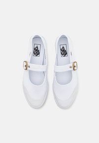 Zapatos Mary Jane de lona blanca con puntera redonda, tira en el mediopié con un hebilla de color dorado y el logo de Vans en la plantilla.