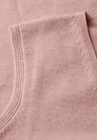 Mjukt rosa stickat tyg som visar detaljerad sömnad och vikta kanter, som framhäver textur och hantverk.