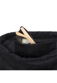 Black corduroy fabric bag with a soft, ribbed texture. A pair of sunglasses with black frames and bamboo arms rests inside.