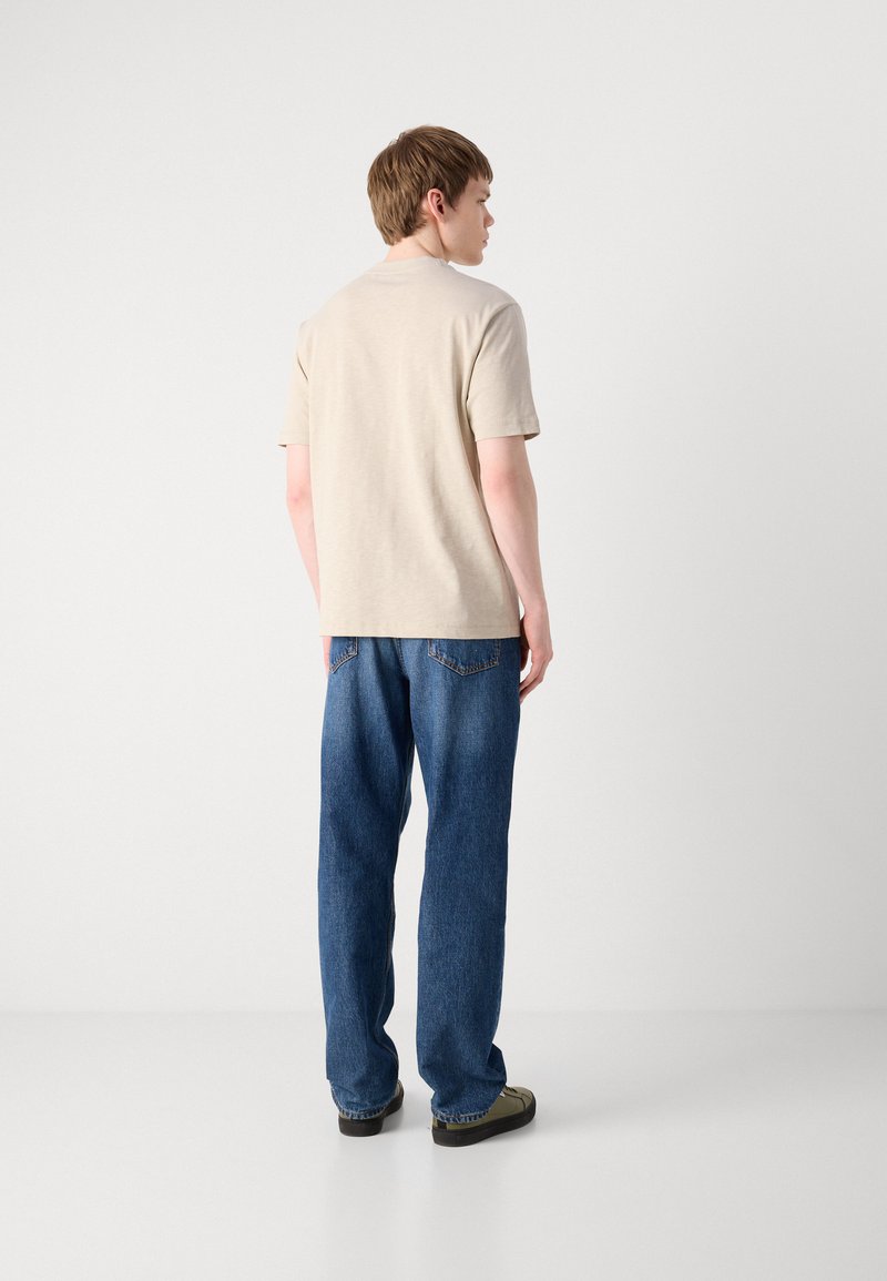 Beżowy t-shirt z krótkim rękawem, wykonany z bawełny, w połączeniu z luźnymi niebieskimi dżinsami. Gładka tekstura i casualowy design.