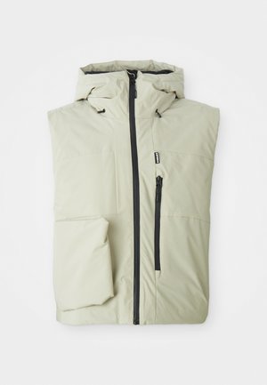 Casaco bege sem mangas, acolchoado, com fecho à frente, capuz e bolso no peito com fecho, dobrado cuidadosamente sobre um fundo branco.