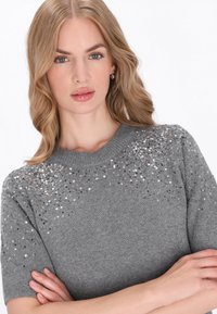 Pulover gri cu mânecă scurtă, cu un guler rotund, decorat cu paiete care strălucesc, având un design tricotat texturat.