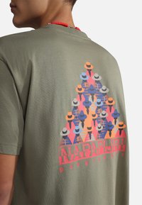 Camiseta de algodón verde oliva con un gráfico multicolor de sombreros dispuestos en un patrón triangular y el texto "NAPAPIJRI geographic".