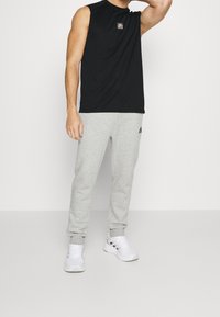Black sleeveless shirt with logo, gray sweatpants, and white sneakers. Casual athletic wear with a simple design and comfortable fit.