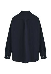 Camicia nera a maniche lunghe vista da dietro con una piega centrale sulla schiena e polsini con bottoni su sfondo bianco.