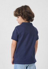 Marineblauwe polo met korte mouwen en een kraag, gecombineerd met lichte spijkerbroekshorts. Gemaakt van zacht katoen, eenvoudig ontwerp, geen zichtbare patronen.