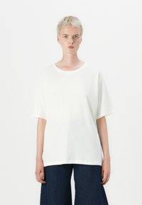 Hvid bomulds t-shirt med korte ærmer, rund hals og en afslappet pasform, parret med mørke denim brede bukser.