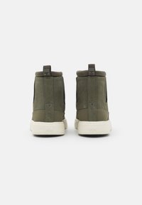 Green suede ankle boots with a soft collar, elastic side panels, and a white rubber sole. Features a logo tag on the back.