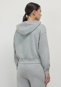 Sweat à capuche gris en matériau doux. Il possède des manches longues, des poignets côtelés et une coupe à la taille. Design simple, sans logos visibles.