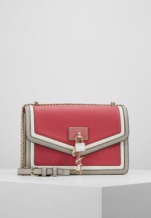 Sac à main en cuir rouge et crème avec une bandoulière en chaîne, doté d'une fermeture magnétique, de quincaillerie dorée et d'un charm décoratif.
