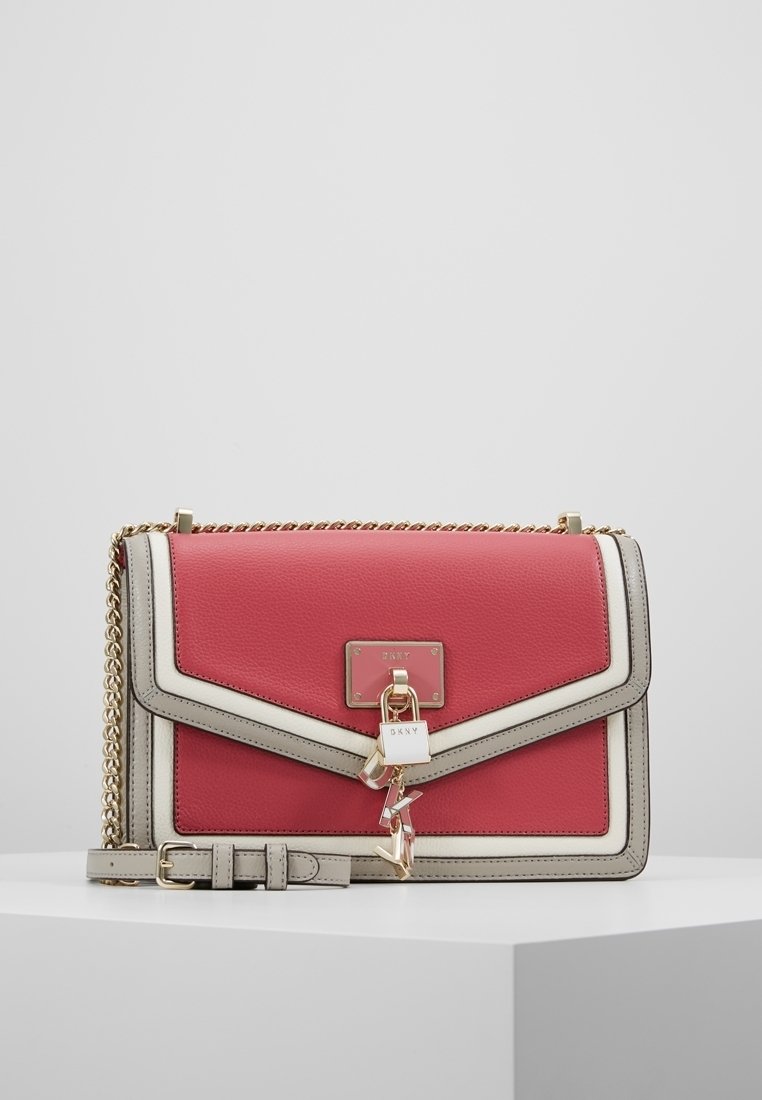 Sac à main en cuir rouge et crème avec une bandoulière en chaîne, doté d'une fermeture magnétique, de quincaillerie dorée et d'un charm décoratif.