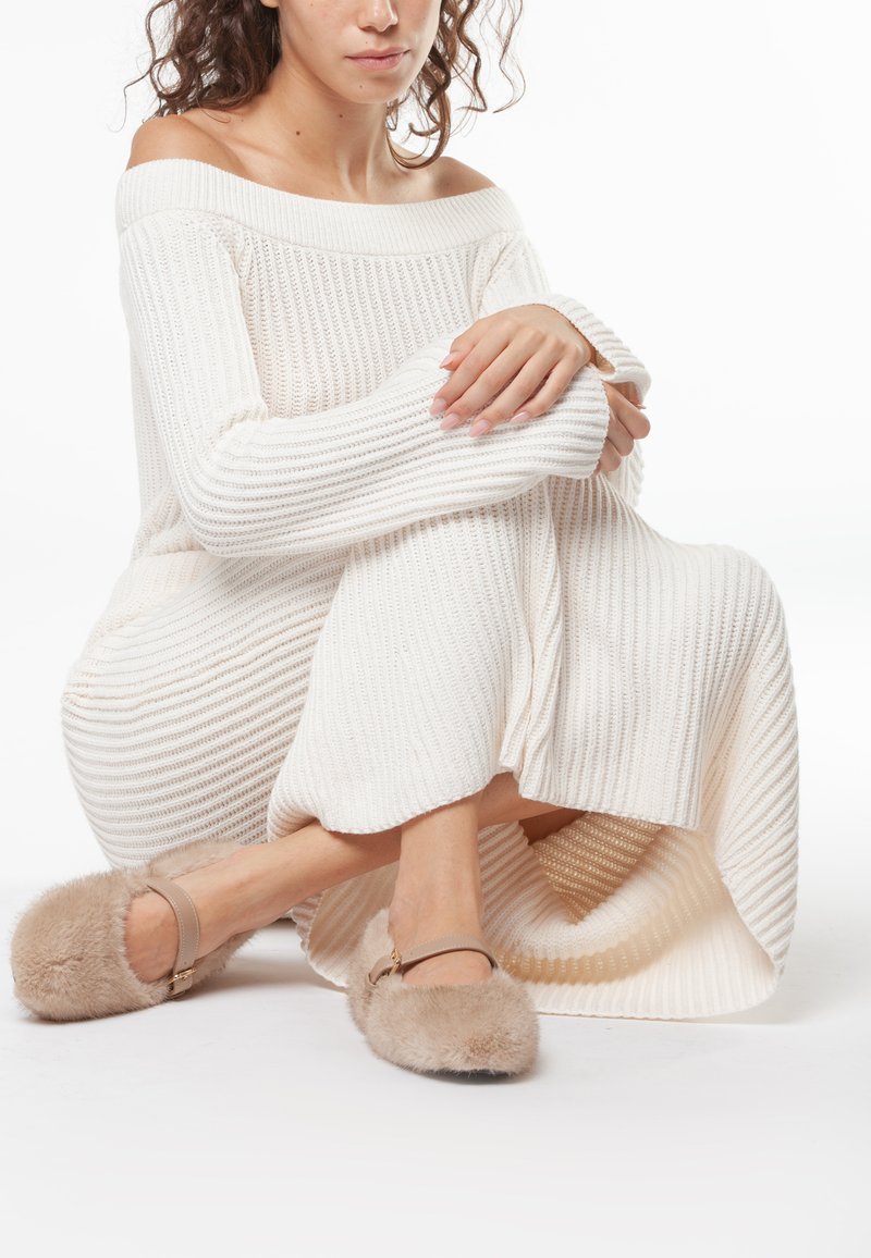 Abito in maglia crema off-the-shoulder con texture a coste, abbinato a pantofole beige soffici con cinturino e dettagli in oro.