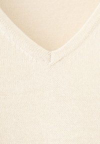 Gros plan d’un tissu tricoté couleur crème montrant un décolleté en V avec une couture côtelée détaillée sur le bord.