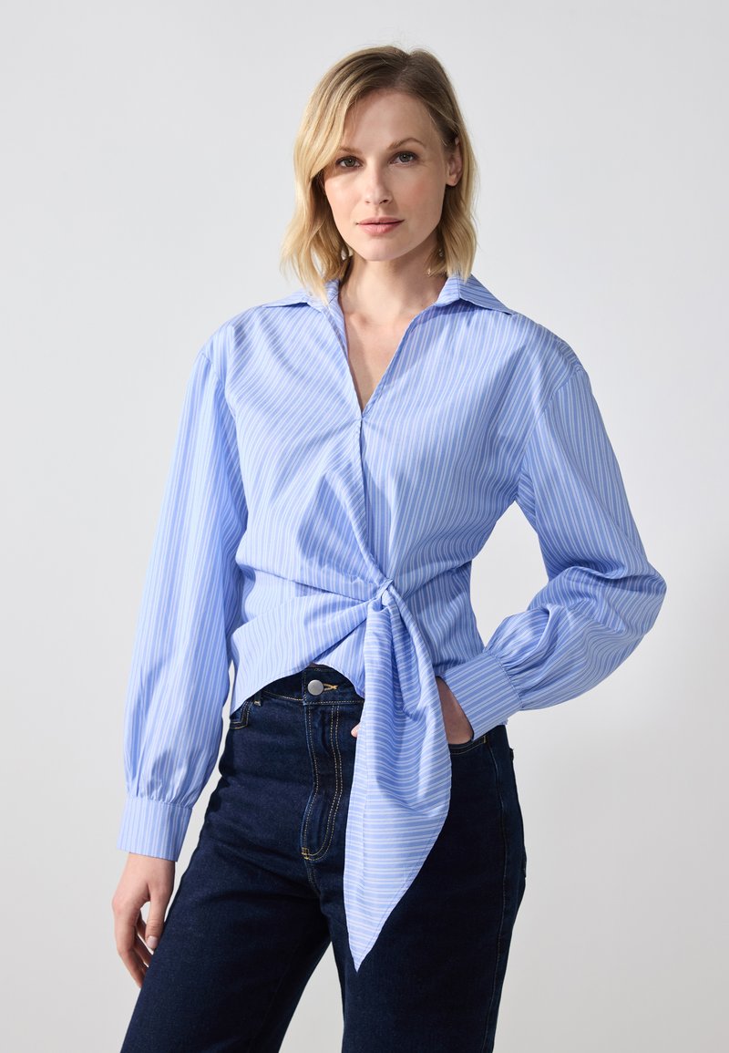 Lyseblå stripete skjorte med lange ermer, krage og knute-detalj foran, sammen med mørke jeans. Glatt stoff med en avslappet passform.