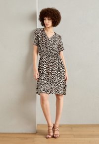 Robe portefeuille imprimée léopard en beige et marron, avec des manches courtes et une taille à nouer. Une paire de sandales à lanières marron clair est présentée avec.