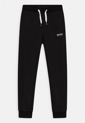 Pantalones de chándal negros hechos de una tela suave, con un cordón blanco, aberturas en las piernas ajustadas y un pequeño logo blanco en el muslo izquierdo.