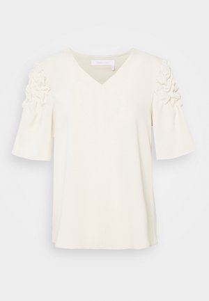 Blouse crème à encolure en V et manches courtes bouffantes avec des détails de tissu froncé sur les épaules.