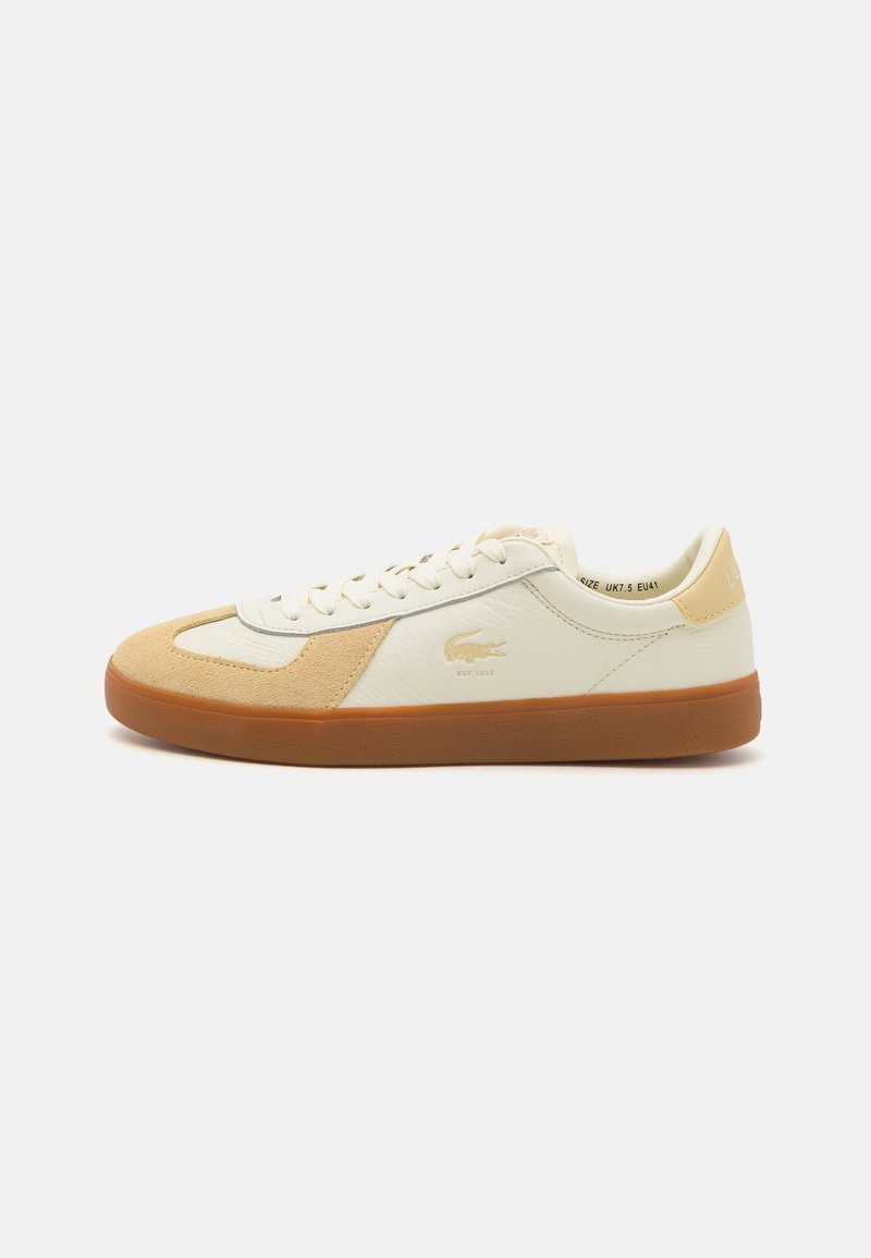 White and beige low-top sneaker with gum sole, lace-up design, and small crocodile logo on side.