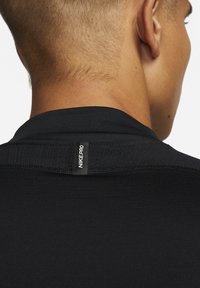 Nahaufnahme eines Nackens mit kurzem Haar, der ein schwarzes Nike Pro Shirt trägt, das den gestickten Kragen und das Logo-Tag zeigt.