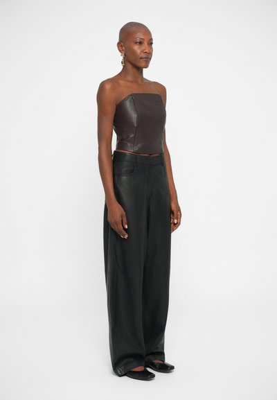 Bruine leren strapless top gecombineerd met wijde zwarte leren broek. Soepele textuur en op maat gemaakt ontwerp, met platte zwarte schoenen.