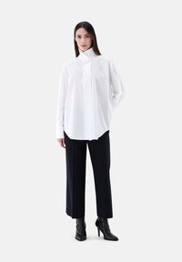 Camicia bianca con colletta alta, maniche lunghe e vestibilità comoda, abbinata a pantaloni larghi blu navy e stivali neri con tacco.