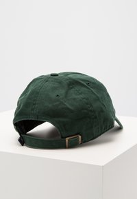 Casquette de baseball en coton vert avec une visière incurvée, une sangle réglable et une texture subtile. Elle possède des trous de ventilation et un design classique.
