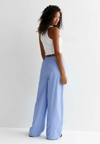 Pantalons à larges rayures bleu clair avec une taille élastique, associés à un débardeur blanc ajusté, avec une texture lisse.