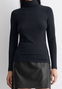 Top a collo alto nero a maniche lunghe realizzato in tessuto liscio, design aderente, abbinato a una mini gonna in pelle nera. Estetica minimalista.