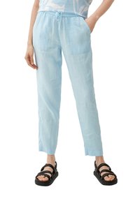 Lichtblauwe linnen broek met een elastische tailleband en trekkoord, voorzien van twee voorzakken en een tapered leg ontwerp. Gedomineerd met zwarte sandalen.