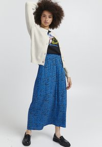 Cardigan beige claro, camiseta gráfica negra y falda larga azul con estampado de leopardo negro. Los mocasines negros completan el conjunto.