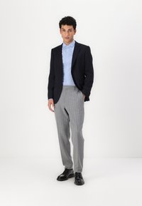 Ναυτικό σακάκι, ανοιχτό μπλε πουκάμισο με γιακά, γκρι παντελόνι με ρίγες, και μαύρα παπούτσια. Σαφής εφαρμογή με δομημένο σχέδιο και διακριτή υφή.