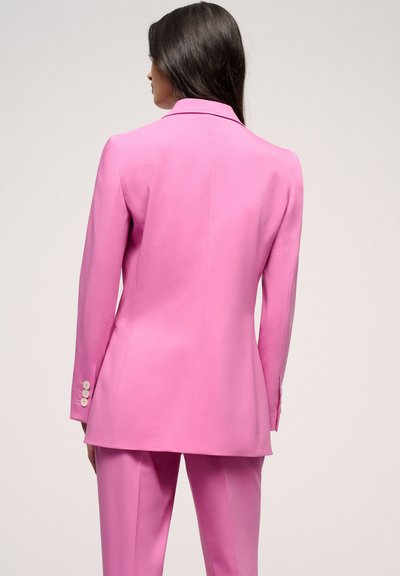 Pink blazer and trousers in a smooth, tailored fabric. Features a notched collar and three-button cuffs. Solid color, no patterns.
