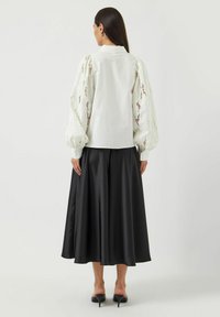 Hvit bluse med blonde-puffermer, kombinert med et svart sateng A-linje skjørt og nudefargede høyhælte sandaler. Glatt tekstur, elegant design.
