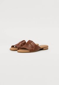 Sandali scivolati in pelle marrone con cinturini incrociati e punta aperta. Suola piatta con tacco minimo. Superficie testurizzata e dettagli in grana naturale.