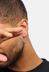 Silberner Creolenohrring mit einem Rosenanhänger, der am Ohr hängt und durch filigrane Details sowie eine polierte Oberfläche besticht.