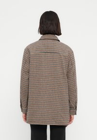 Καρό πουκάμισο-σακάκι σε καφέ και μαύρο, με γιακά, μακριά μανίκια και χαλαρή εφαρμογή. Διαθέτει μία ενίσχυση στο πίσω μέρος.