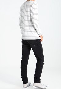 Bílé tričko s dlouhým rukávem a černými pruhy, v kombinaci s černými džínami a bílými teniskami. Tričko má kulatý výstřih a pohodlný střih.