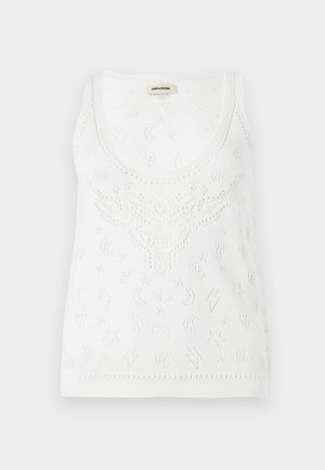 Mujer con gafas de sol, top blanco sin mangas, falda larga marrón con cordones, botas marrones, llevando un gran bolso marrón de ante al hombro.