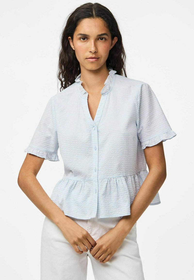 Blusa azzurra a quadretti con maniche corte, colletto arricciato, chiusura con bottoni e orlo a peplum. Realizzata in cotone con una finitura testurizzata.