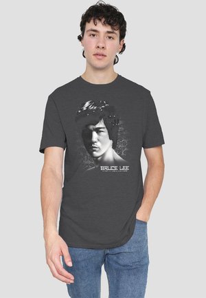 Dunkelgraues T-Shirt mit einem schwarz-weißen Grafikmotiv von Bruce Lees Gesicht, das eine detaillierte Haarzeichnung zeigt, und weißem Text darunter.