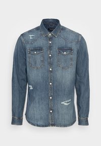 Keski sininen farkkupaita, jossa on kaksi rintataskua, napilliset painonapit, länsityylinen vuori ja kuluneita yksityiskohtia edessä.