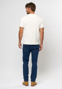 Hvid ribbet kortærmet t-shirt, parret med blå jeans og brune støvler. Simpelt design, tætsiddende form og struktureret stof.