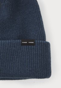 Navy ribbed knit beanie with a folded cuff, featuring a black rectangular tag with the text "SAMSOE SAMSOE" in white.