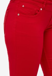 Punaiset stretch-farkut, joissa on sileä pinta, suunniteltu etutaskulla ja hopeisilla yksityiskohdilla. Ominaisuuksiin kuuluu istuva, kapeneva lahkeen muoto.