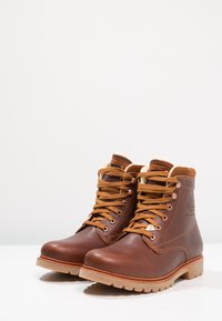 Botas de cuero marrón con cordones en tono cuero claro, un forro suave y una suela resistente. Presenta un logo en relieve y ojales de metal para un ajuste seguro.