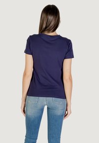 T-shirt in cotone blu navy con collo rotondo e maniche corte, abbinato a jeans aderenti azzurri, che mostrano una texture liscia e un design casual.