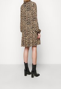 Femme portant une robe imprimé léopard midi à manches longues et des bottines noires à talons hauts, debout sur un fond blanc.