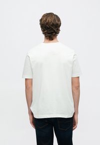 Λευκό βαμβακερό t-shirt με κοντά μανίκια και στρογγυλή λαιμόκοψη, με άνετη εφαρμογή και ομαλή υφή, συνδυασμένο με σκούρο μπλε τζιν.