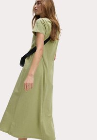 Světle zelené šaty do poloviny stehen s krátkými rukávy, volný střih a jemná textura. Spárované s černou crossbody taškou.
