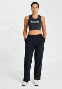 Sportowy biustonosz w ciemnoszarym kolorze z białym logo; elastyczna talia czarnych spodni z bocznymi kieszeniami; luźny krój; gładka faktura.